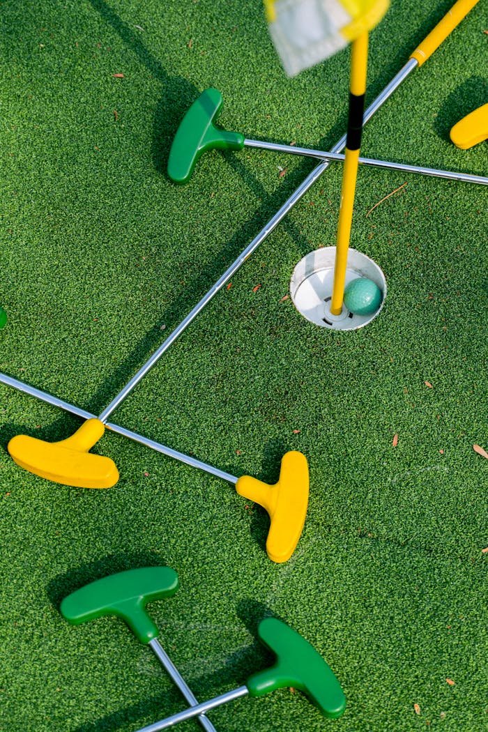 Colorful mini golf putters arranged around a hole on a vibrant green putting surface.